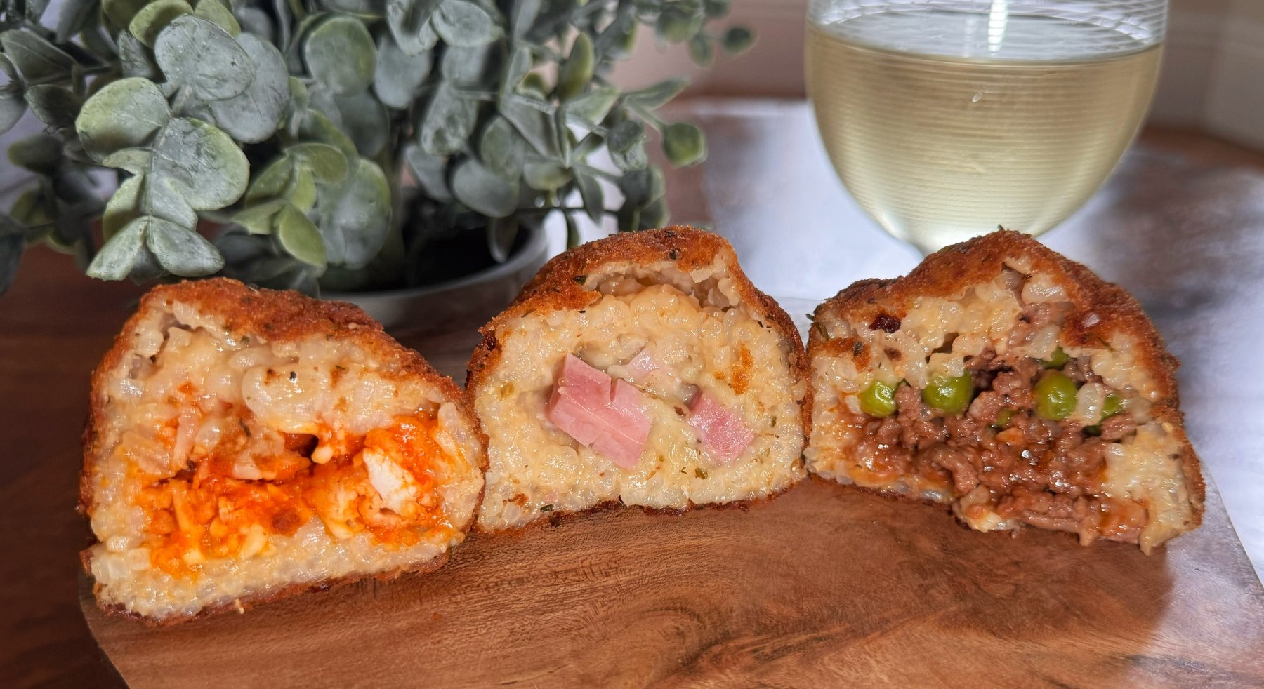 Three arancini halves showing the traditional beef and pea, ham and cheese, and buffalo chicken fillings